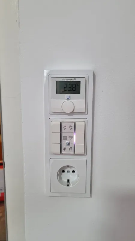 Homematic-IP-Wandthermostat und Sechsfach-Taster über einer Steckdose