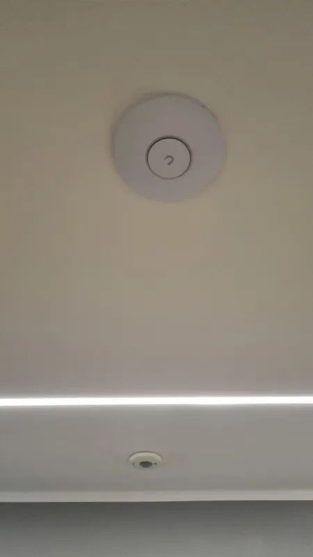 Runder UniFi-Access-Point an der Decke über einer indirekten Lichtlinie
